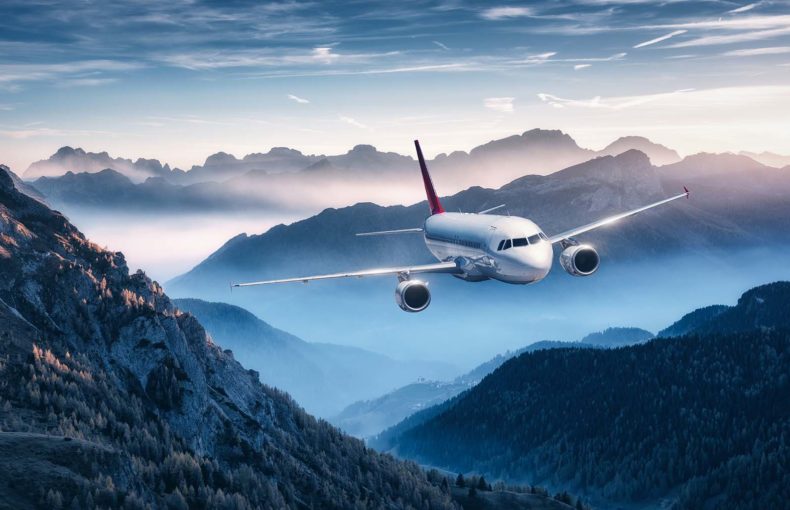 Airplane flying over mountains in fog at sunset in summer
