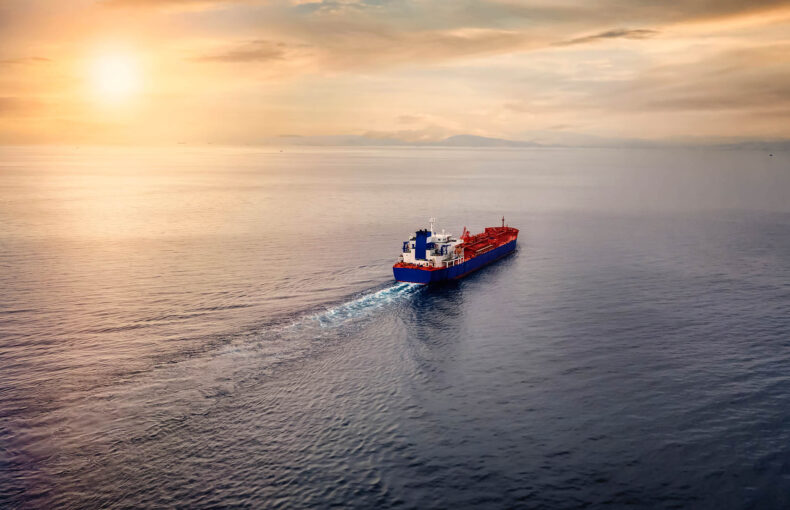 Aerial view of a container cargo ship sailing over calm sea into the sunset
