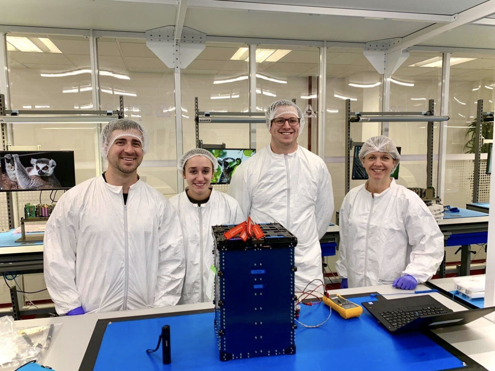 Zoe Clark posing behind a Spire Global LEMUR satellite