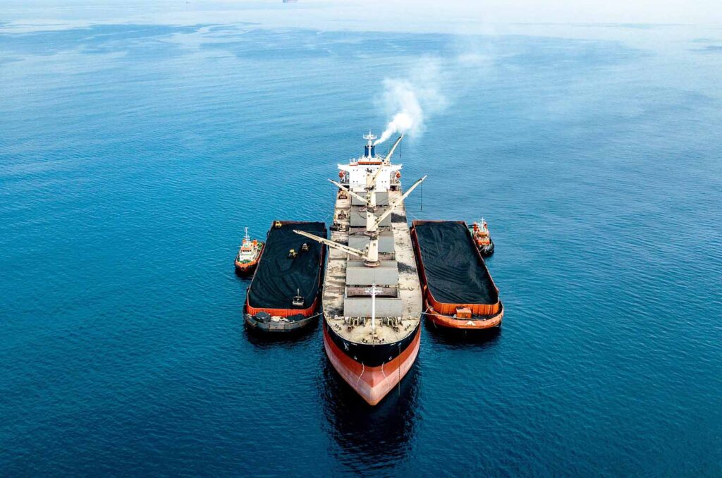 Shipping vessel at sea with assisting barge tug boats