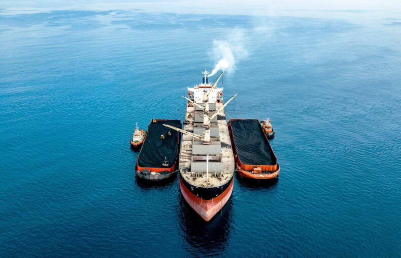 Shipping vessel at sea with assisting barge tug boats